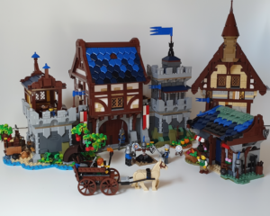 LEGO medieval village scene with large buildings, a cart pulled by a horse, minifigures, and detailed surroundings including trees, flags, and a market stall. Showcasing an alternate lego build.